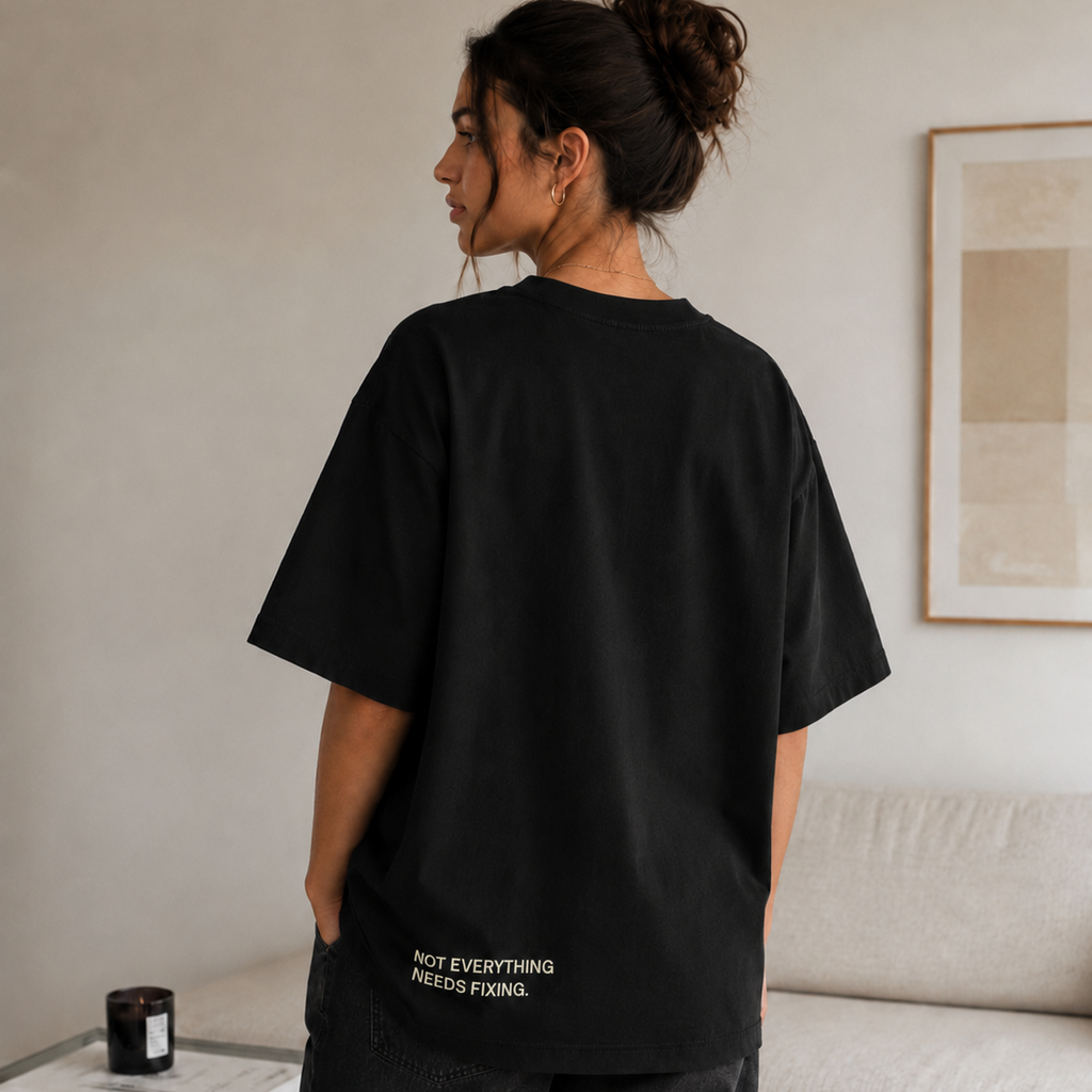 Person wearing a black t-shirt with text in a room with a couch and books.