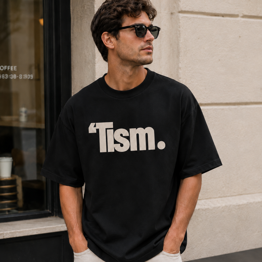 Man wearing a black t-shirt with 'Tism.' text standing outside a building.