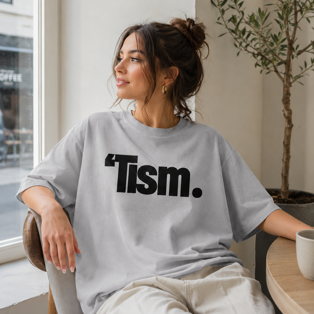 Woman wearing a gray t-shirt with 'Tism.' text in a casual setting.