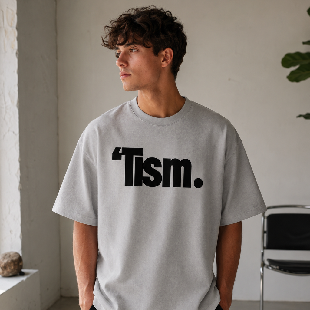 Person wearing a gray t-shirt with 'Tism.' printed on it in a minimal indoor setting.